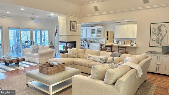 living room with a towering ceiling, a large fireplace, ceiling fan, light hardwood / wood-style floors, and ornamental molding