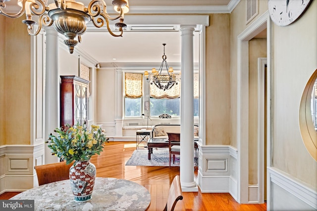 dining area featuring a notable chandelier, light parquet floors, ornamental molding, and decorative columns