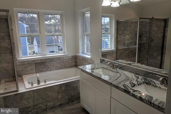 bathroom with tiled bath, vanity, and a notable chandelier