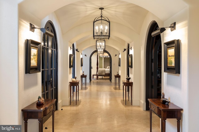 hallway featuring french doors, vaulted ceiling, and an inviting chandelier