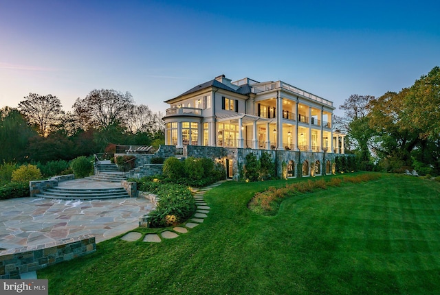 back house at dusk with a yard, a balcony, and a patio