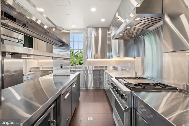 kitchen featuring stainless steel counters, dark tile patterned flooring, stainless steel appliances, and wall chimney range hood