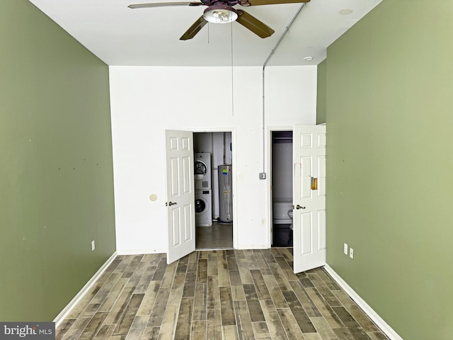 unfurnished bedroom featuring electric water heater, ceiling fan, stacked washer / dryer, a high ceiling, and dark hardwood / wood-style floors