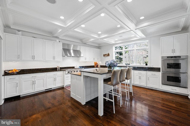 kitchen featuring white cabinetry, a center island, stainless steel appliances, wall chimney range hood, and a breakfast bar area