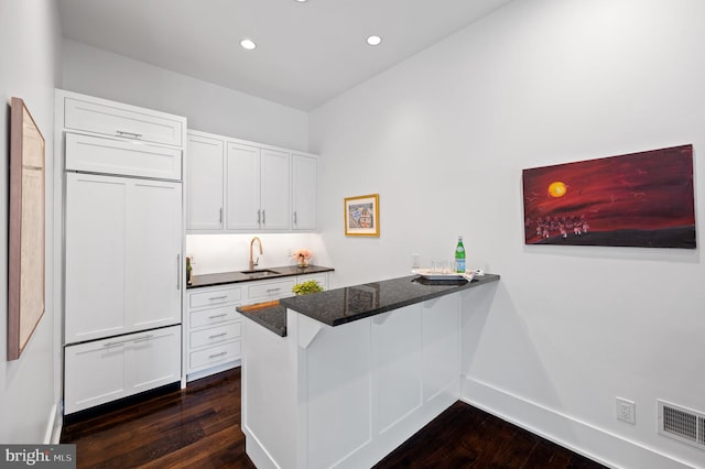 kitchen featuring dark stone counters, kitchen peninsula, sink, dark hardwood / wood-style floors, and white cabinetry