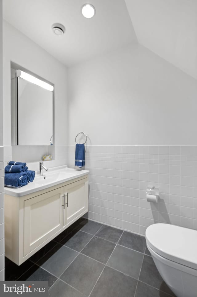 bathroom with vanity, vaulted ceiling, tile patterned flooring, toilet, and tile walls