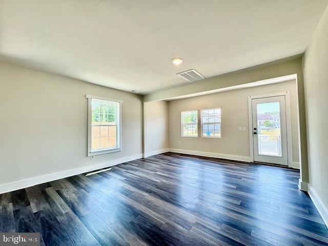 empty room with a wealth of natural light and dark hardwood / wood-style flooring