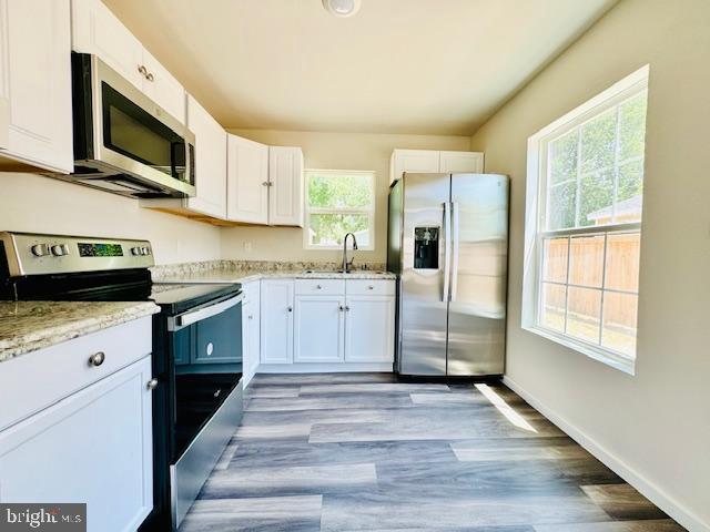 kitchen with white cabinets, sink, light stone countertops, a healthy amount of sunlight, and stainless steel appliances