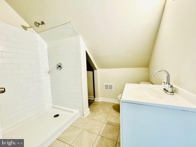 bathroom with tile patterned flooring, toilet, lofted ceiling, and a tile shower