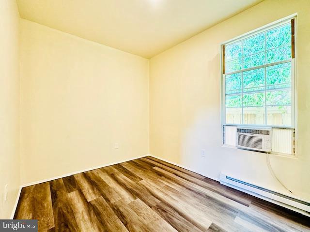 empty room with wood-type flooring and a baseboard heating unit