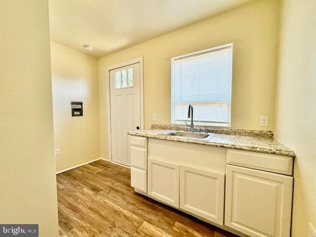 kitchen featuring white cabinets, light stone counters, light wood-type flooring, and sink