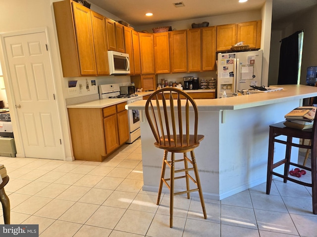 kitchen with a kitchen island with sink, light countertops, white appliances, and a breakfast bar