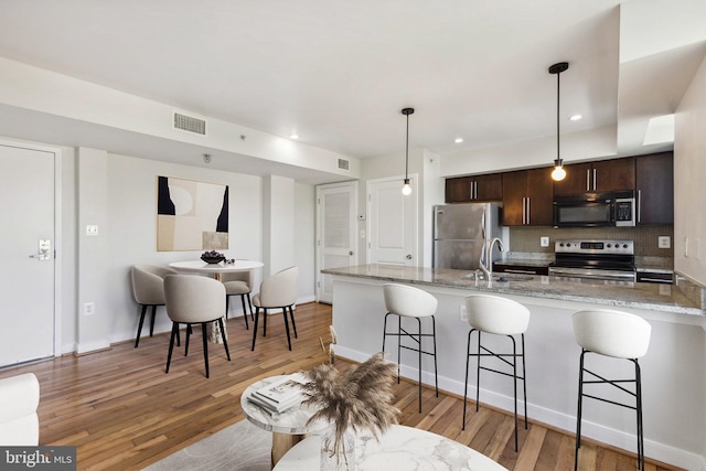 kitchen with dark brown cabinets, stainless steel appliances, sink, light hardwood / wood-style flooring, and hanging light fixtures