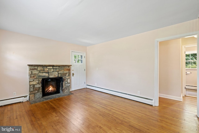 unfurnished living room featuring a stone fireplace, wood-type flooring, and a baseboard heating unit