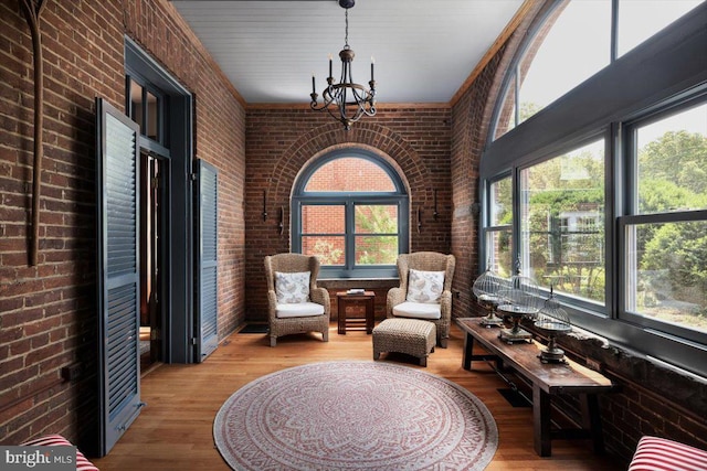 living area featuring an inviting chandelier, hardwood / wood-style flooring, and brick wall