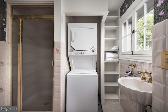 laundry room featuring tile patterned flooring, stacked washing maching and dryer, and sink