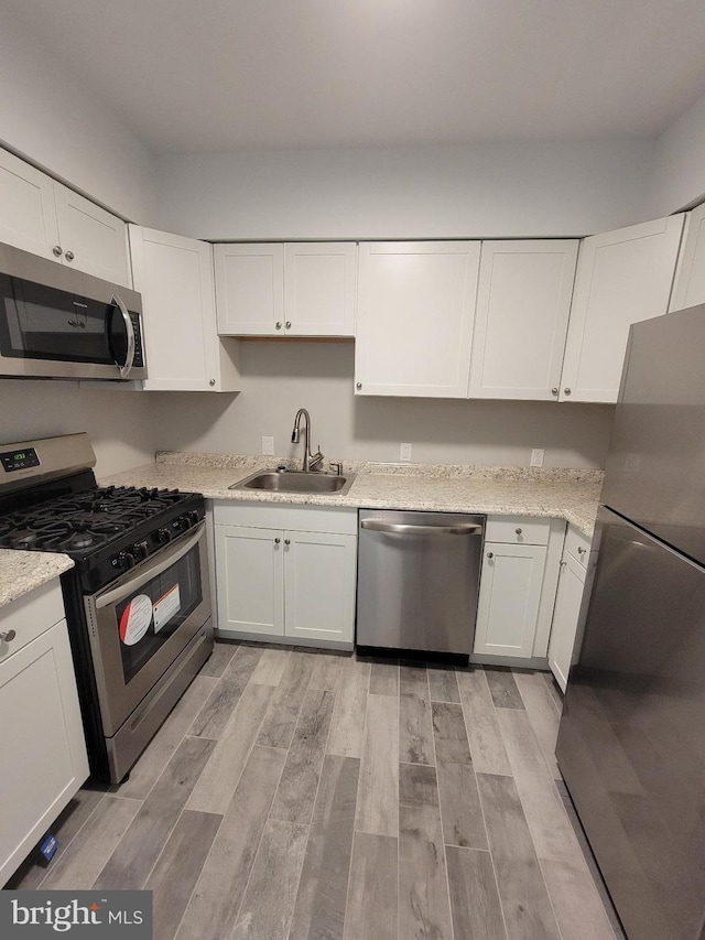 kitchen with white cabinetry, sink, stainless steel appliances, and light hardwood / wood-style flooring