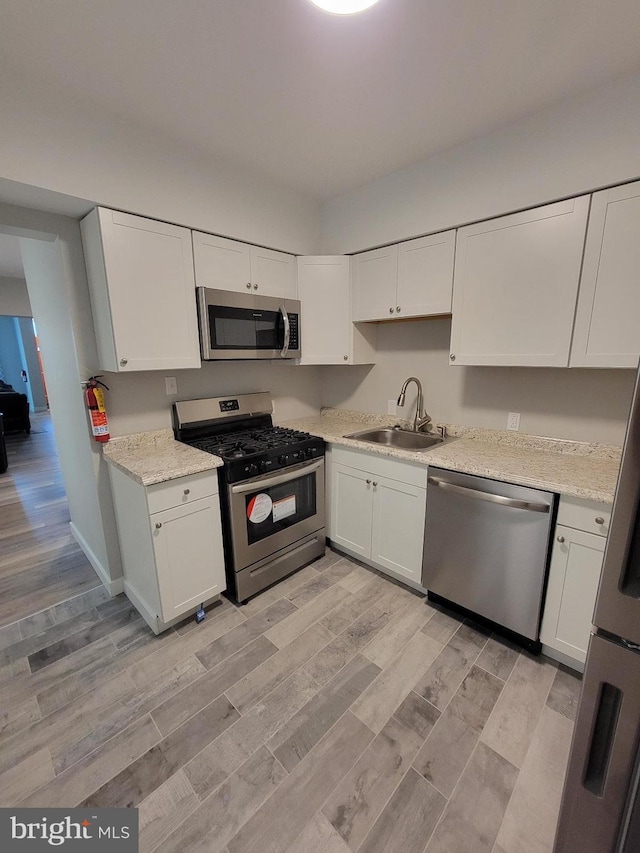 kitchen with sink, white cabinets, light hardwood / wood-style flooring, and appliances with stainless steel finishes