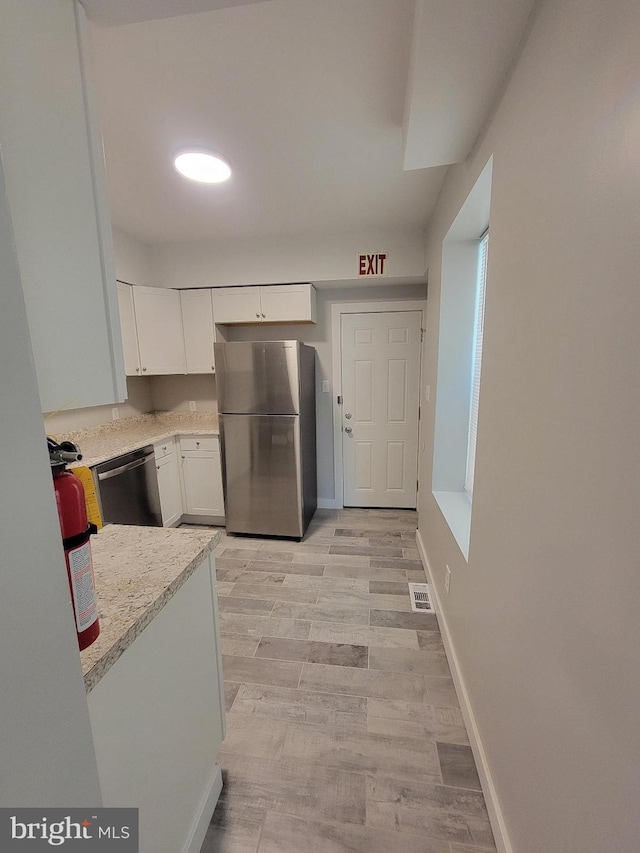 kitchen with white cabinets, light wood-type flooring, stainless steel appliances, and light stone countertops