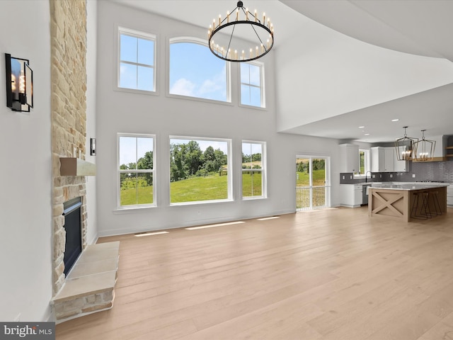 unfurnished living room with a notable chandelier, a stone fireplace, a high ceiling, and light hardwood / wood-style flooring