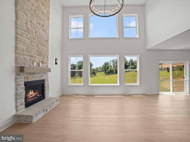 unfurnished living room featuring a stone fireplace, light hardwood / wood-style flooring, a towering ceiling, and a chandelier