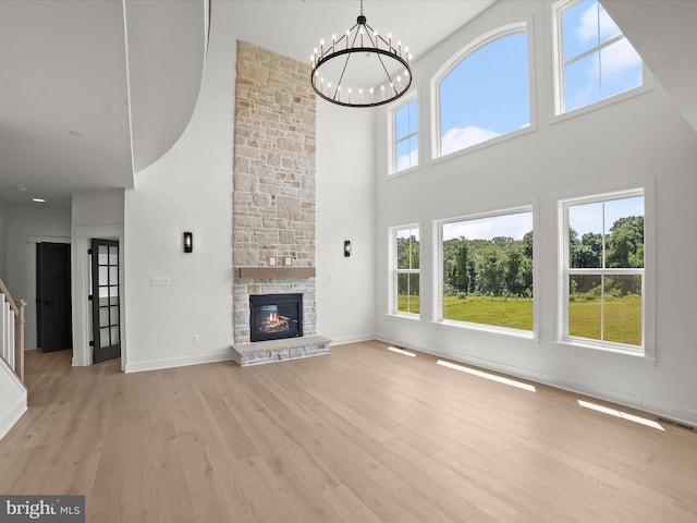 unfurnished living room featuring a high ceiling, light hardwood / wood-style floors, a stone fireplace, and a notable chandelier