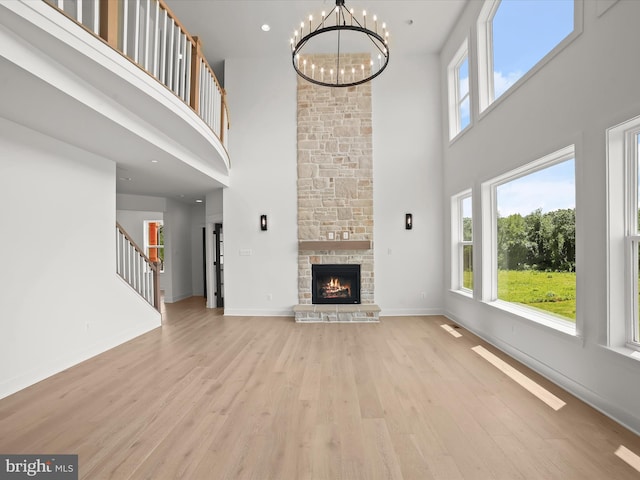 unfurnished living room with a fireplace, a towering ceiling, light hardwood / wood-style flooring, and a notable chandelier