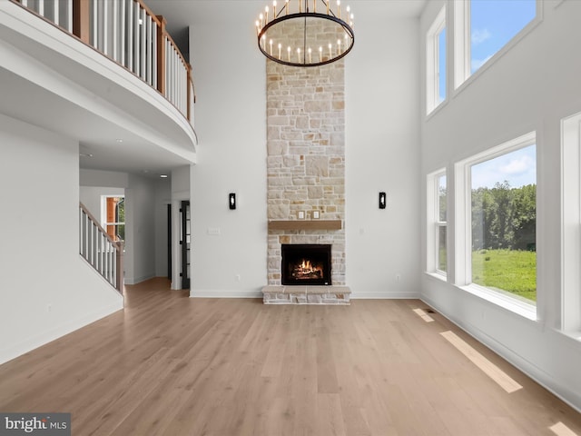 unfurnished living room with a stone fireplace, a towering ceiling, light hardwood / wood-style flooring, and an inviting chandelier