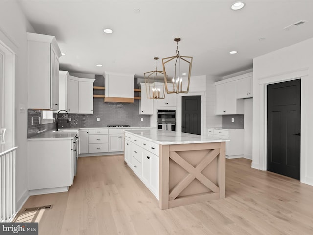 kitchen with a center island, white cabinets, hanging light fixtures, gas stovetop, and light hardwood / wood-style floors