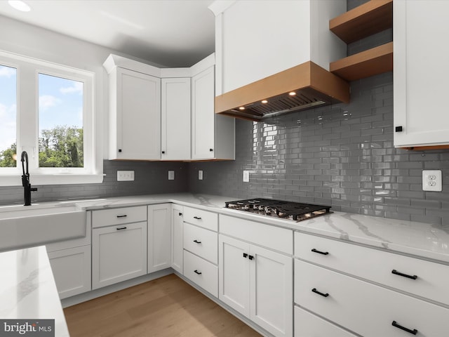 kitchen featuring stainless steel gas stovetop, custom exhaust hood, light stone countertops, tasteful backsplash, and white cabinetry