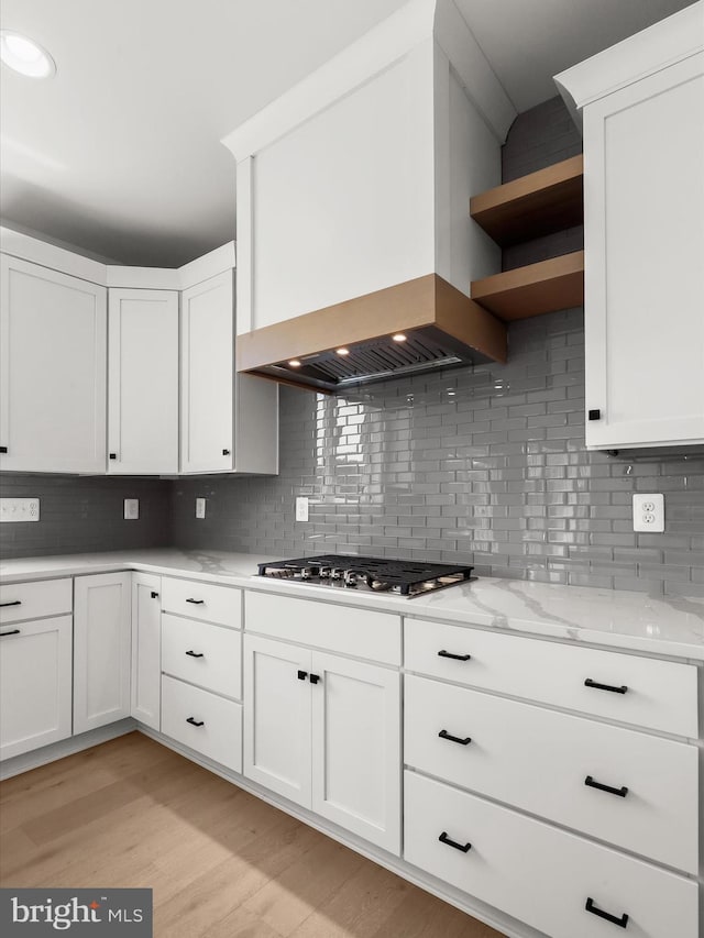 kitchen featuring decorative backsplash, custom range hood, white cabinets, and stainless steel gas cooktop