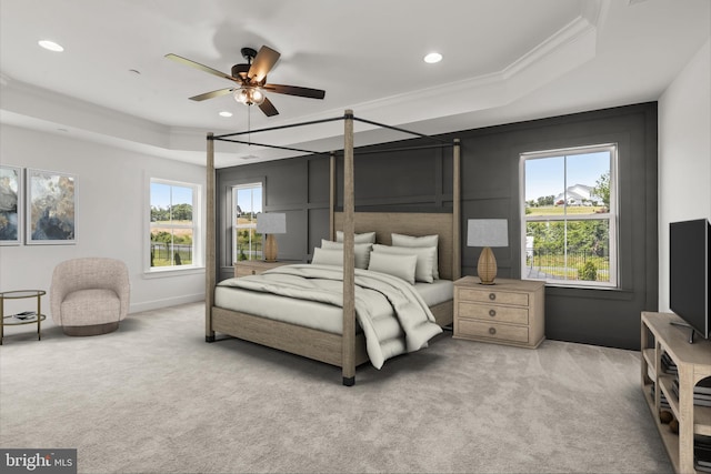 bedroom featuring a tray ceiling, ceiling fan, crown molding, and light carpet