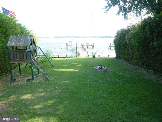 view of yard with a boat dock, a water view, a playground, and an outdoor fire pit