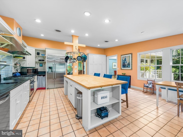 kitchen featuring white cabinets, appliances with stainless steel finishes, wood counters, and light tile patterned flooring