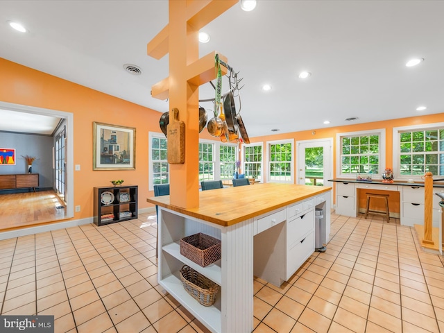 kitchen with a center island, light tile patterned flooring, butcher block countertops, vaulted ceiling, and white cabinets