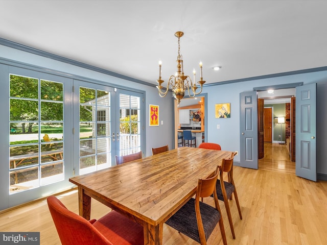 dining space with crown molding, light hardwood / wood-style flooring, french doors, and a notable chandelier