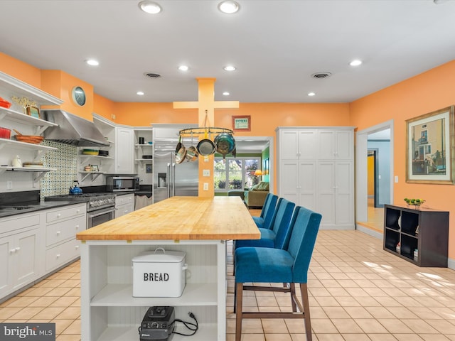 kitchen featuring a center island, high end appliances, white cabinets, decorative backsplash, and butcher block counters