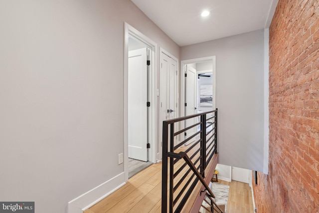 hallway featuring light wood-type flooring and brick wall