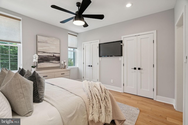 bedroom featuring ceiling fan, light hardwood / wood-style floors, and multiple closets