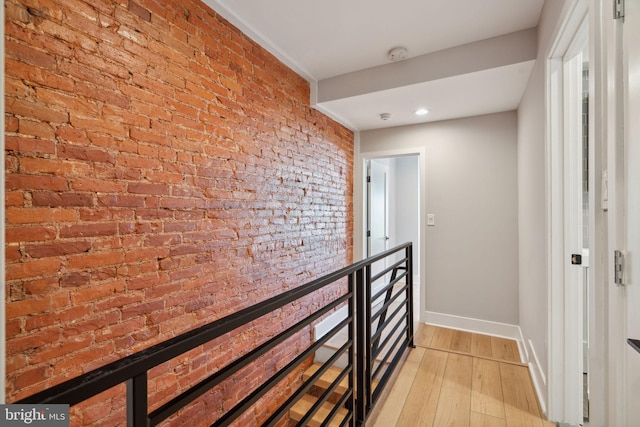 corridor with brick wall and light hardwood / wood-style flooring