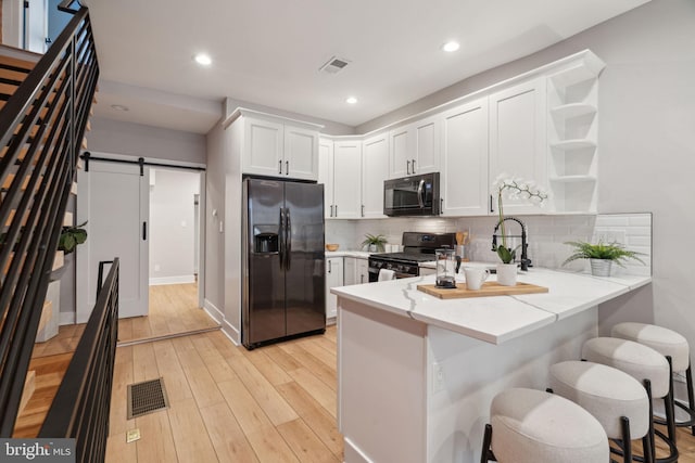 kitchen with a kitchen breakfast bar, black appliances, kitchen peninsula, a barn door, and white cabinets