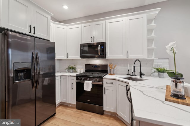 kitchen featuring white cabinets, light stone counters, stainless steel appliances, light hardwood / wood-style floors, and sink