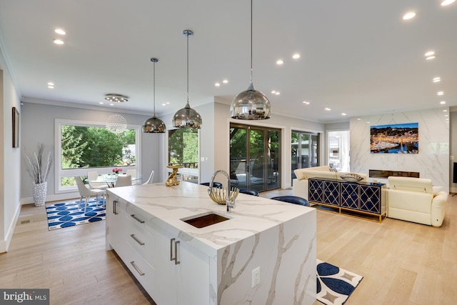 kitchen featuring white cabinets, a center island with sink, sink, decorative light fixtures, and light stone counters