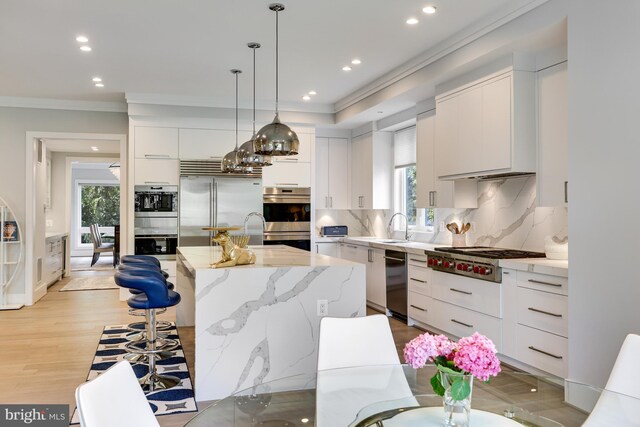 kitchen with pendant lighting, light hardwood / wood-style flooring, a kitchen island, white cabinetry, and stainless steel appliances