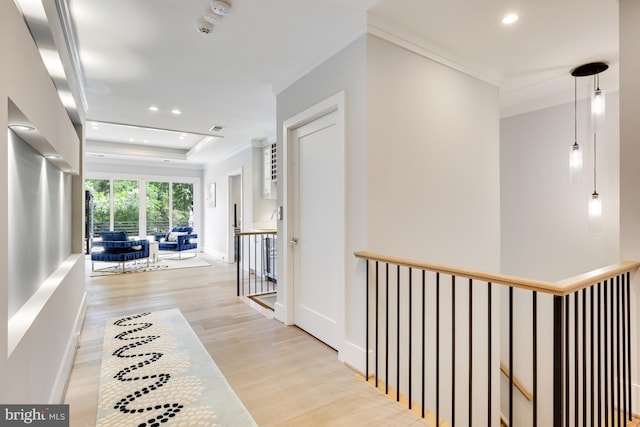 hallway featuring crown molding, a tray ceiling, and light hardwood / wood-style flooring