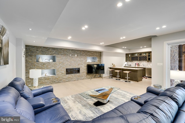 living room featuring light hardwood / wood-style flooring, bar, and a stone fireplace