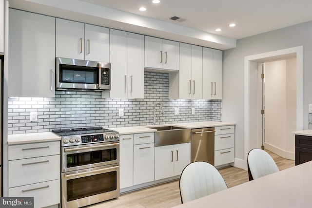 kitchen with sink, backsplash, appliances with stainless steel finishes, white cabinets, and light wood-type flooring