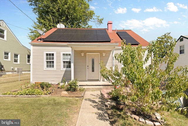 bungalow-style home featuring fence, covered porch, a chimney, a front lawn, and roof mounted solar panels