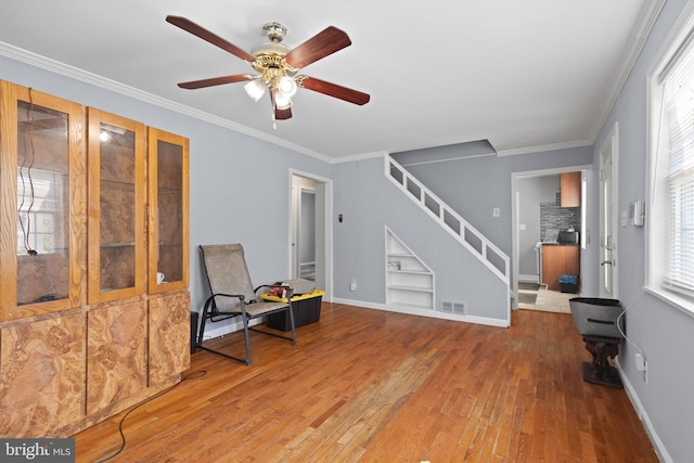 sitting room featuring built in shelves, ceiling fan, ornamental molding, and wood-type flooring