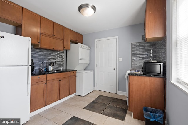 kitchen with light tile patterned flooring, sink, tasteful backsplash, white fridge, and stacked washer / dryer